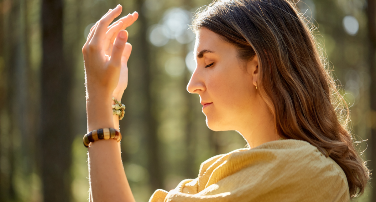 mujer con los brazos frente al rostro y ojos cerrados en el bosque