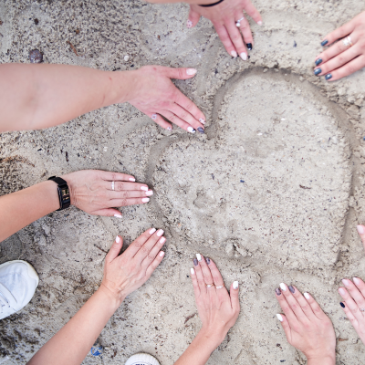 corazón en la arena con manos de mujeres